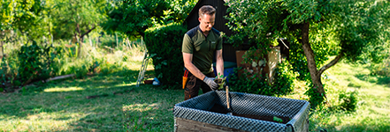 Man in werkkleding plant in een verhoogde tuinbak bij zonnig weer.
