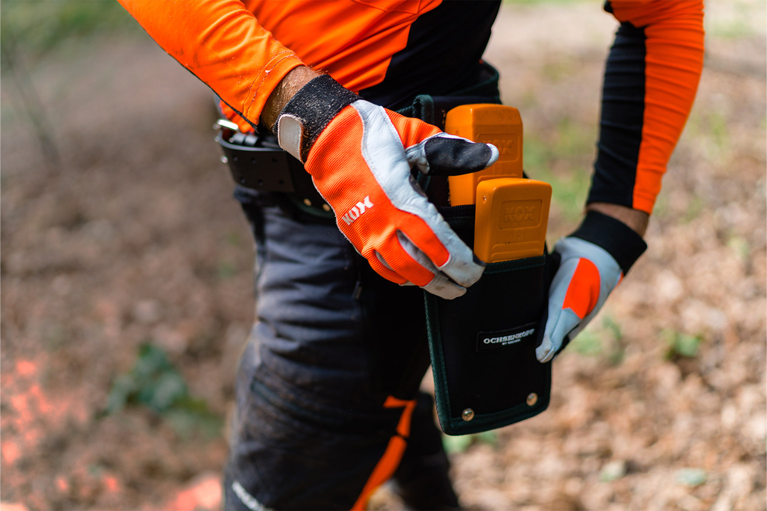 Een persoon in oranje beschermkleding steekt oranje KOX-wiggen in een gereedschapstas aan de riem.